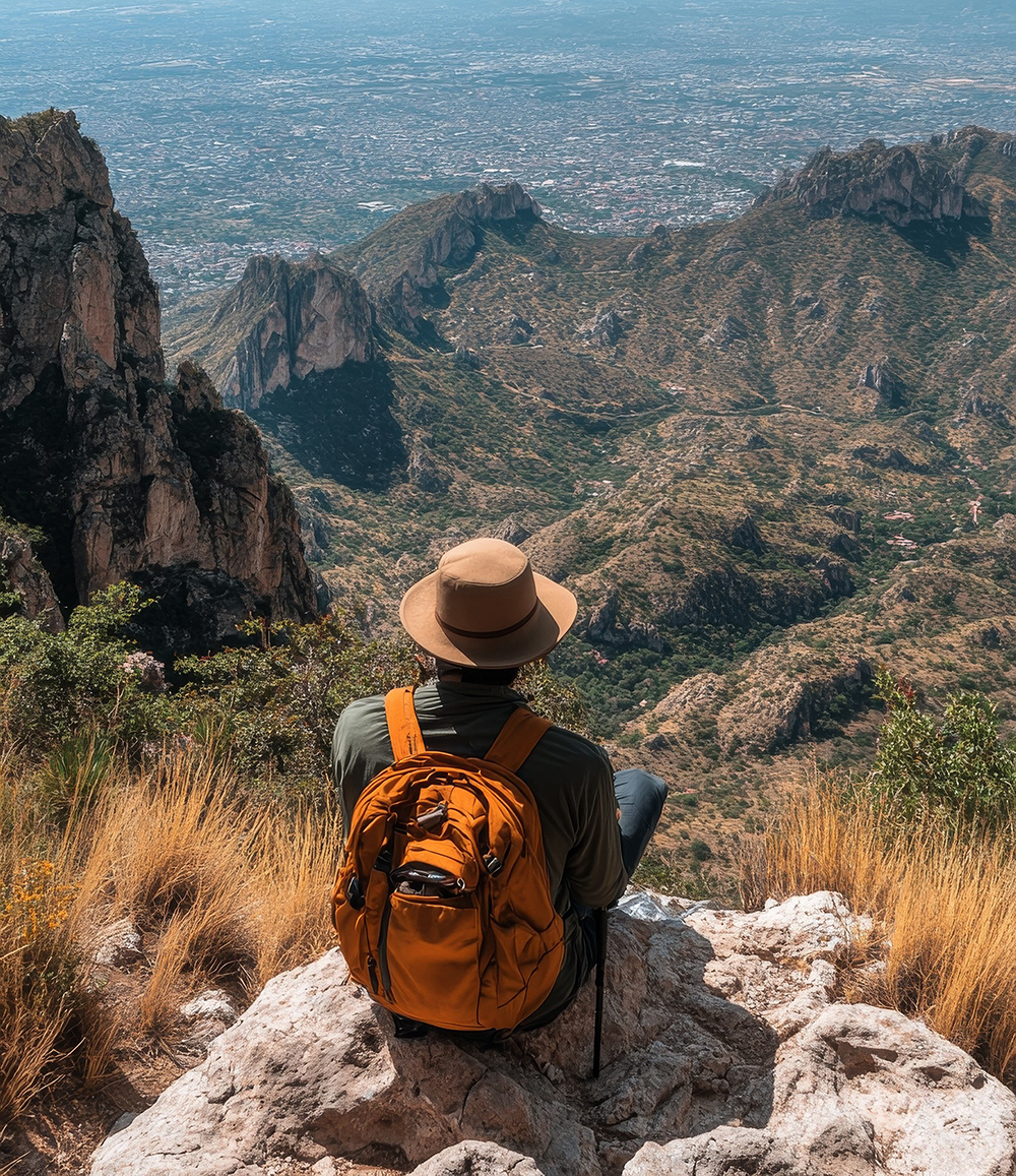 Hiker resting on a rock while overlooking a vast mountain landsc